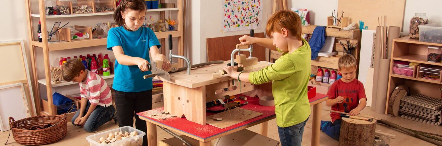 Group of children working together with tools and materials at a shared workshop table.